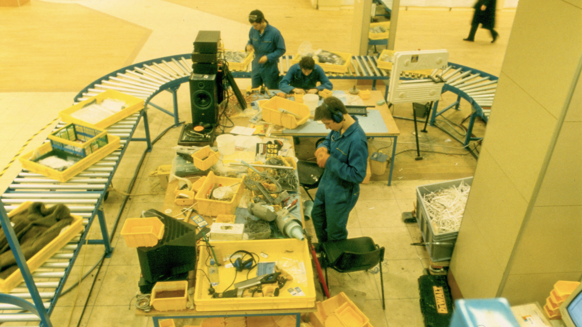 Three people in boilersuits working next to a conveyor belt, dismantling items.
